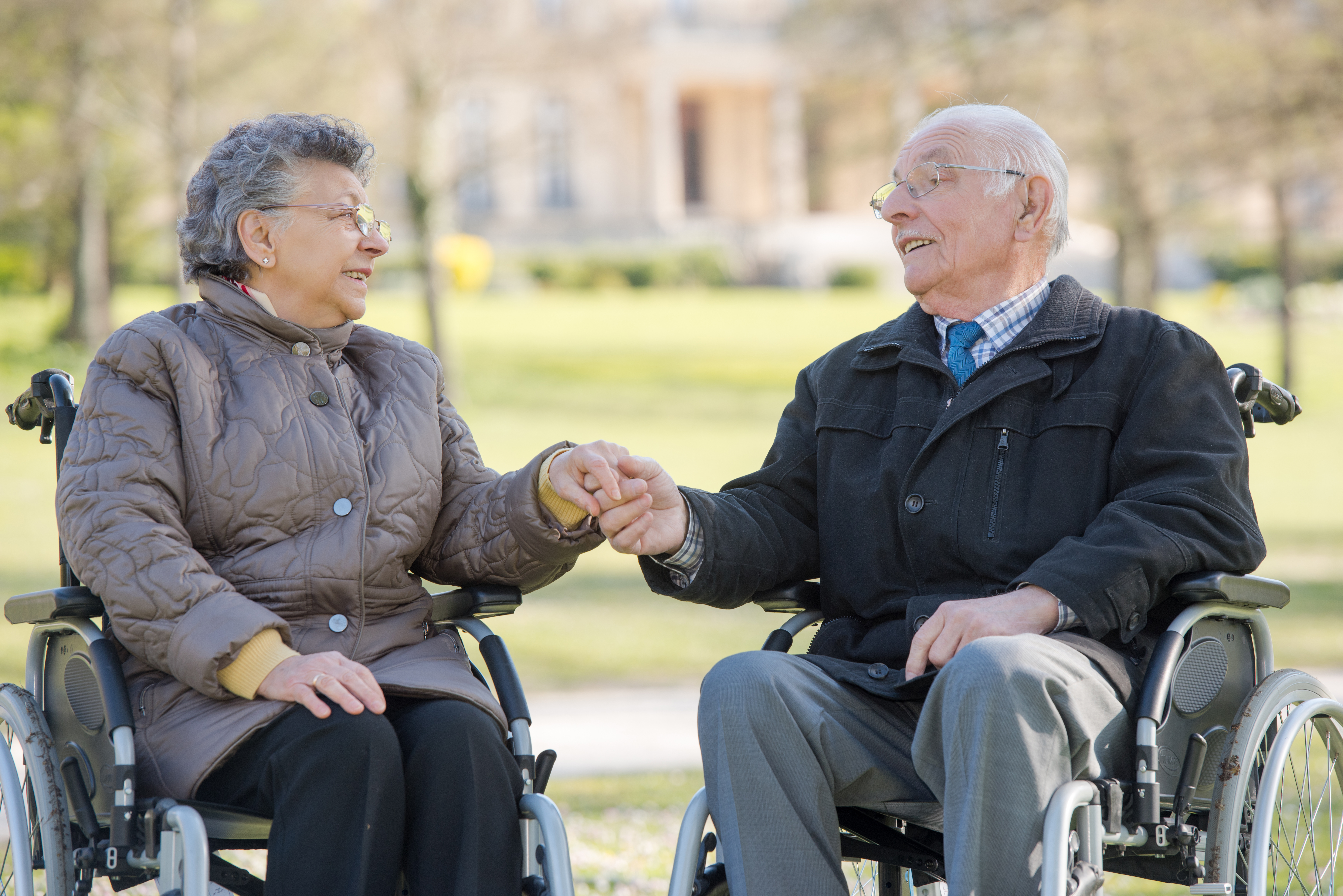 Seniorin und Senior im Rollstuhl halten Hände